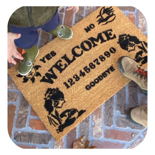 Ouija seance Halloween doormat on a brick patio with a child and mom standing on it