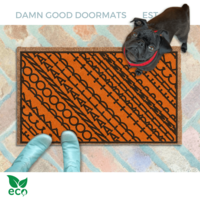 subtle fuck donald trump doormat in abstract contemporary design over a pumpkin orange fall doormat. A pair of feet wearing baby blue boots stands with a black pug dog sitting on the floor next to them. 