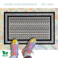 A pair of feet wearing green shoes stands on a subtle patterned FDT Fuck Donald Trump all weather doormat