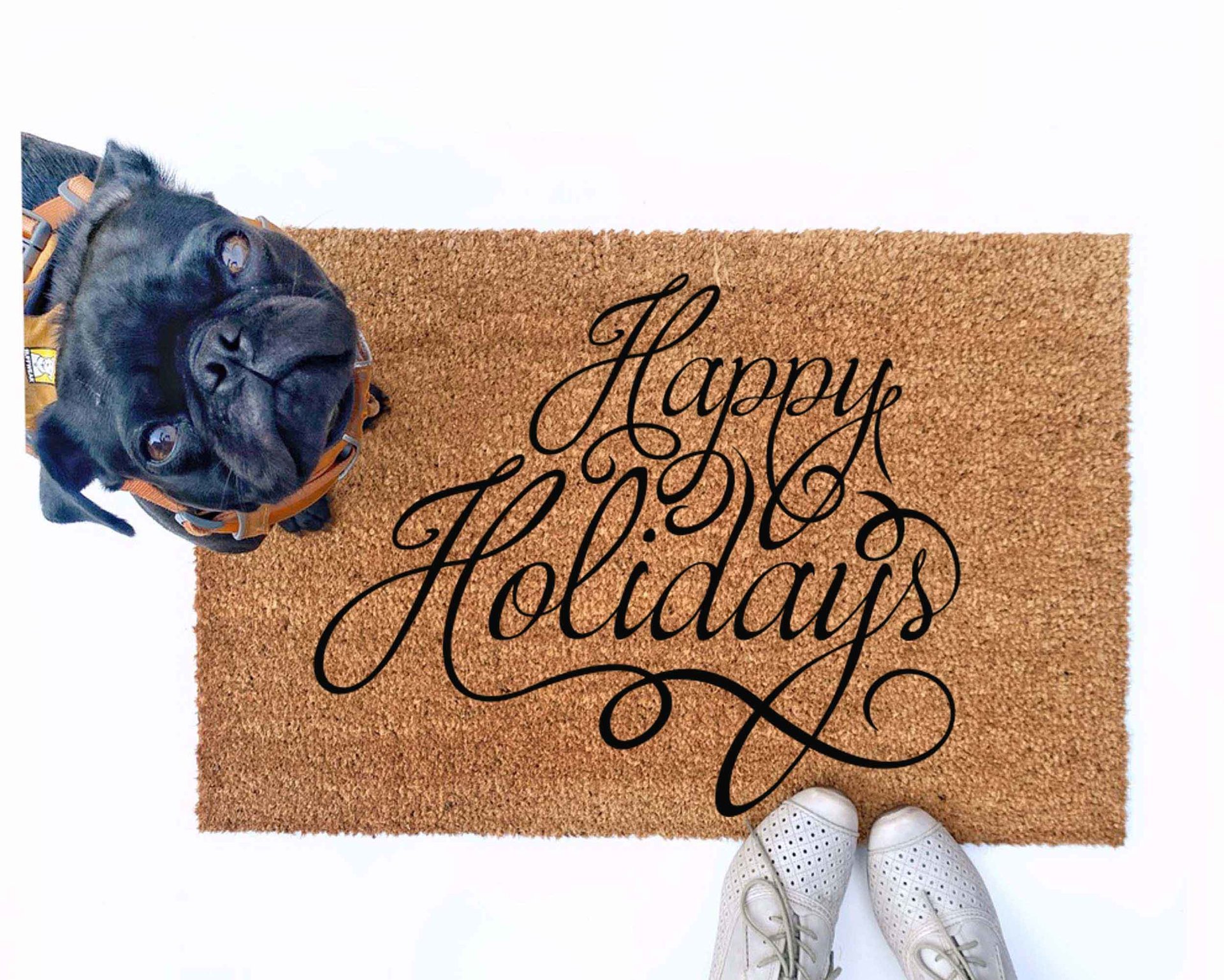 outdoor doormat reading happy holidays in script writing with a black pug puppy