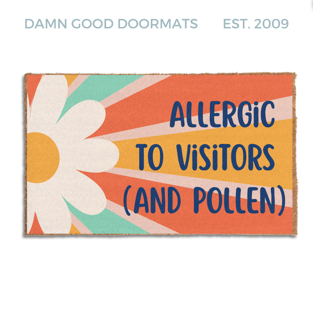 promotional image of a coir doormat reading "Allergic to visitors and pollen" in with a red and yellow 70's hippy flower pattern with graphic stripes all across