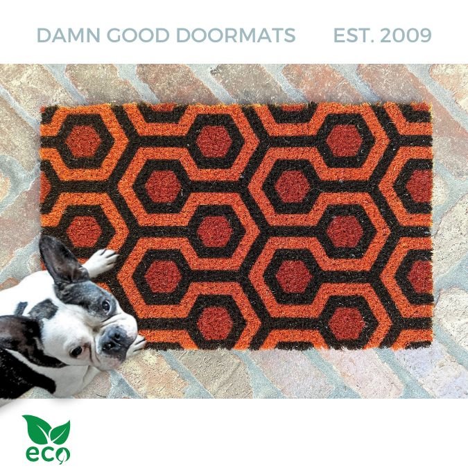 The Shining hex carpet doormat in orange, brown coir welcome mat with retro hexagon design on a brick patio with French Bulldog