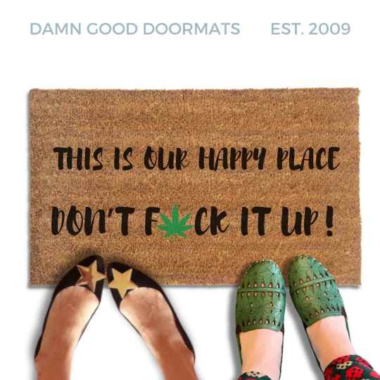 Coir doormat reading "This is our happy place, don't fuck it up," with a green cannabis leaf replacing the U in FUCK. Lifestyle photo shows two pairs of feet standing at the front edge of the mat.